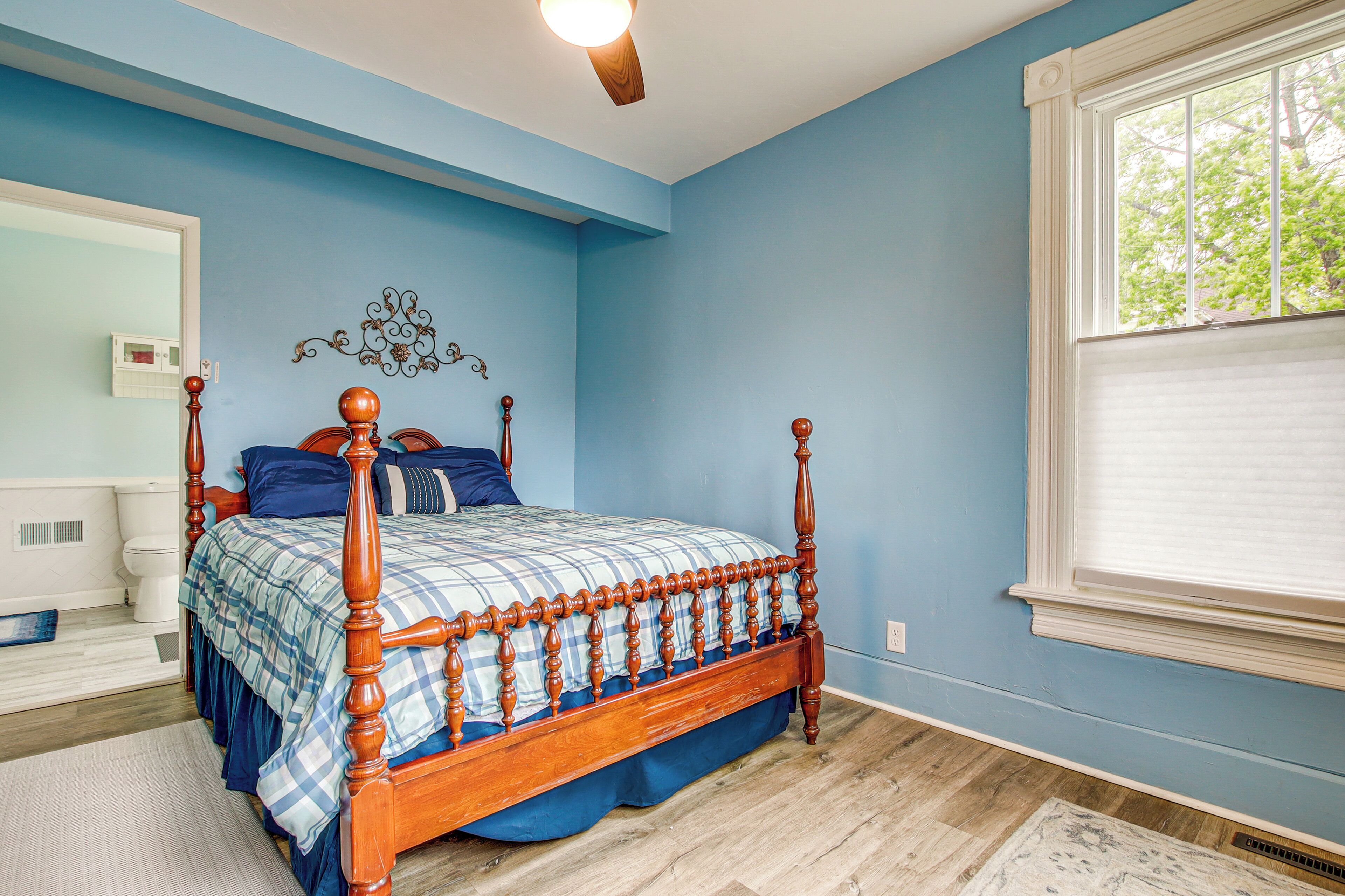 A bedroom with a wooden four-poster bed, a large window with blinds, and a blue wall.