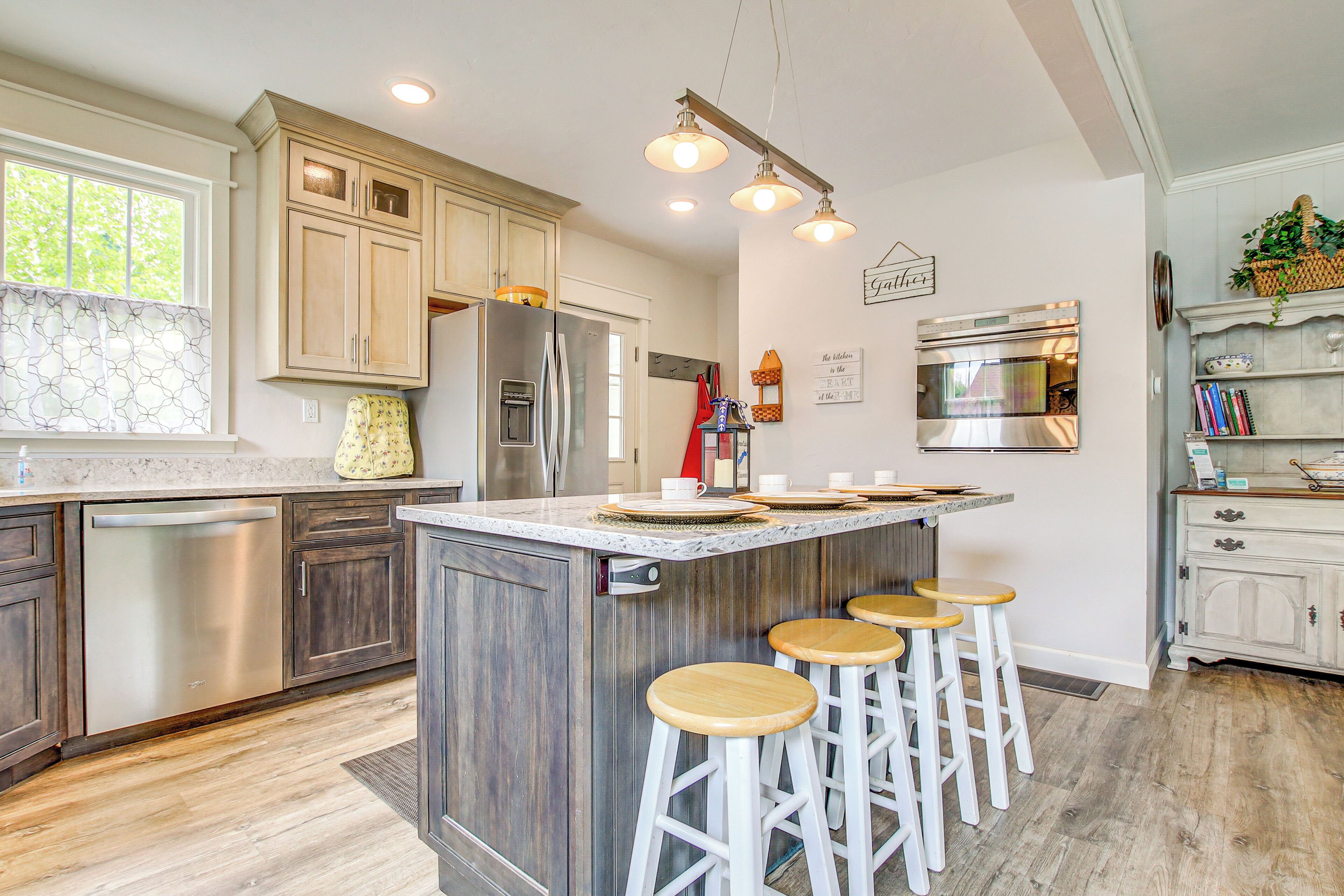A modern kitchen with a central island, bar stools, stainless steel appliances, and wooden cabinetry.