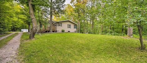A cabin with a deck, surrounded by a grassy yard and trees.