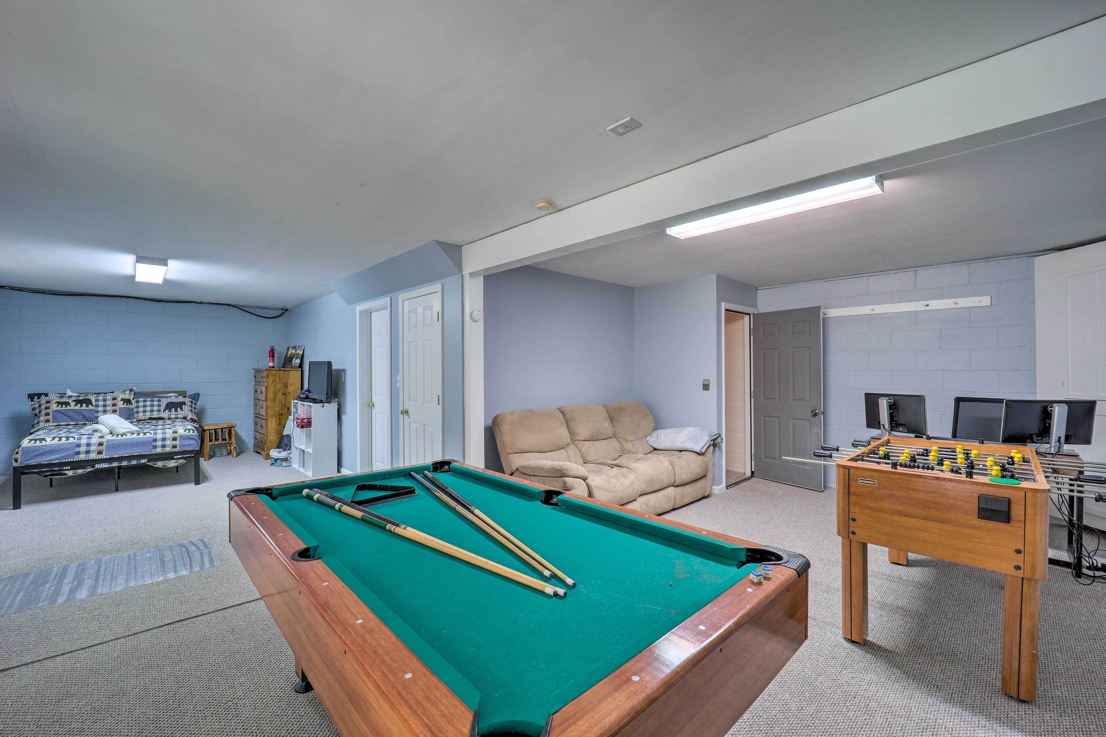 A room with a pool table, a foosball table, a sofa, and a bed.