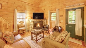 A cozy cabin interior with a fireplace, wooden walls, a television, and comfortable seating. - Fire Pit & Porch: Warm & Woodsy Rothbury Escape! (Rothbury)