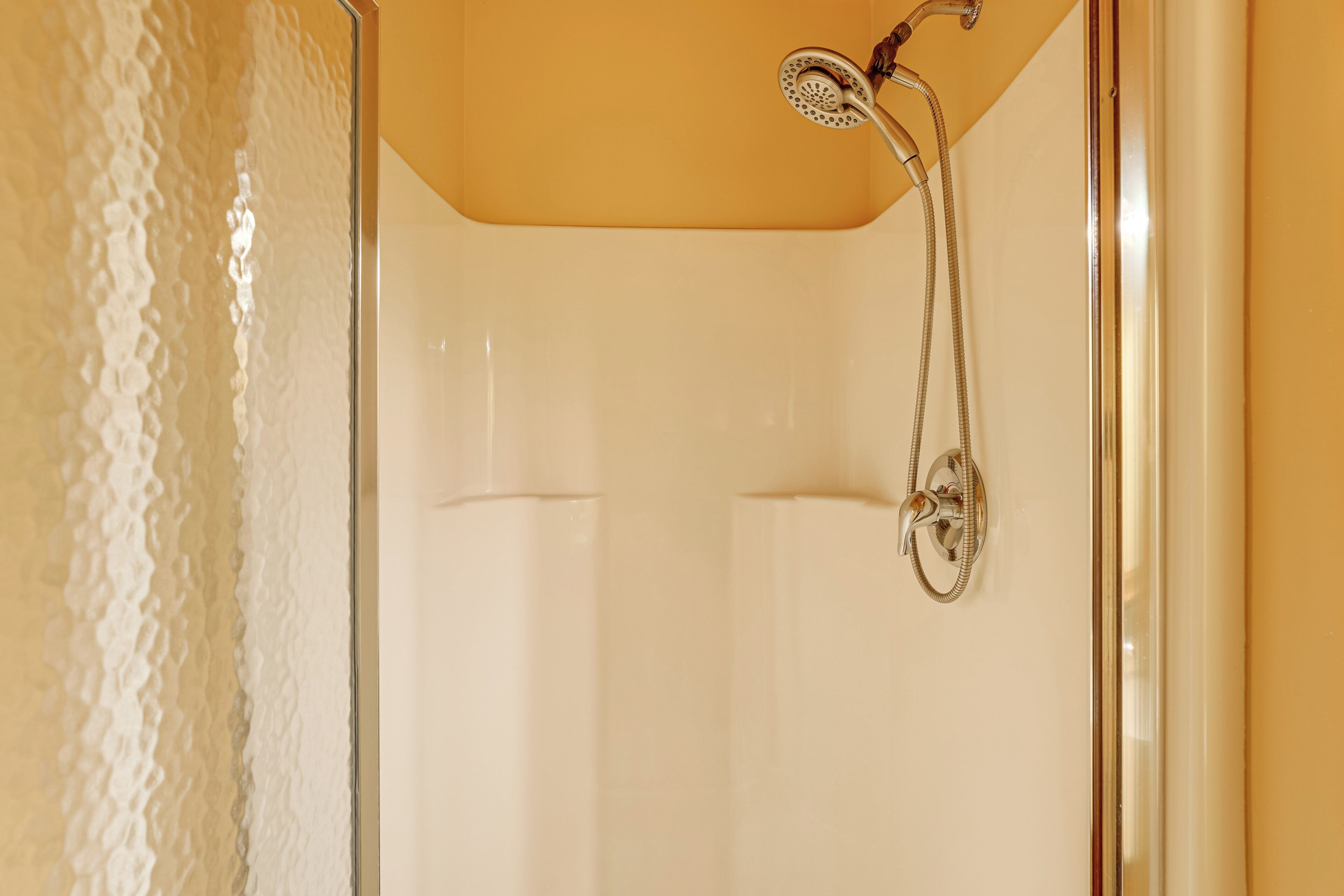 Cabina de ducha con cabezal de ducha de mano y grifería empotrada en la pared.