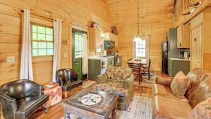 A cozy cabin interior with a dining area, kitchen, and seating arrangements. - Fire Pit & Porch: Warm & Woodsy Rothbury Escape! (Rothbury)