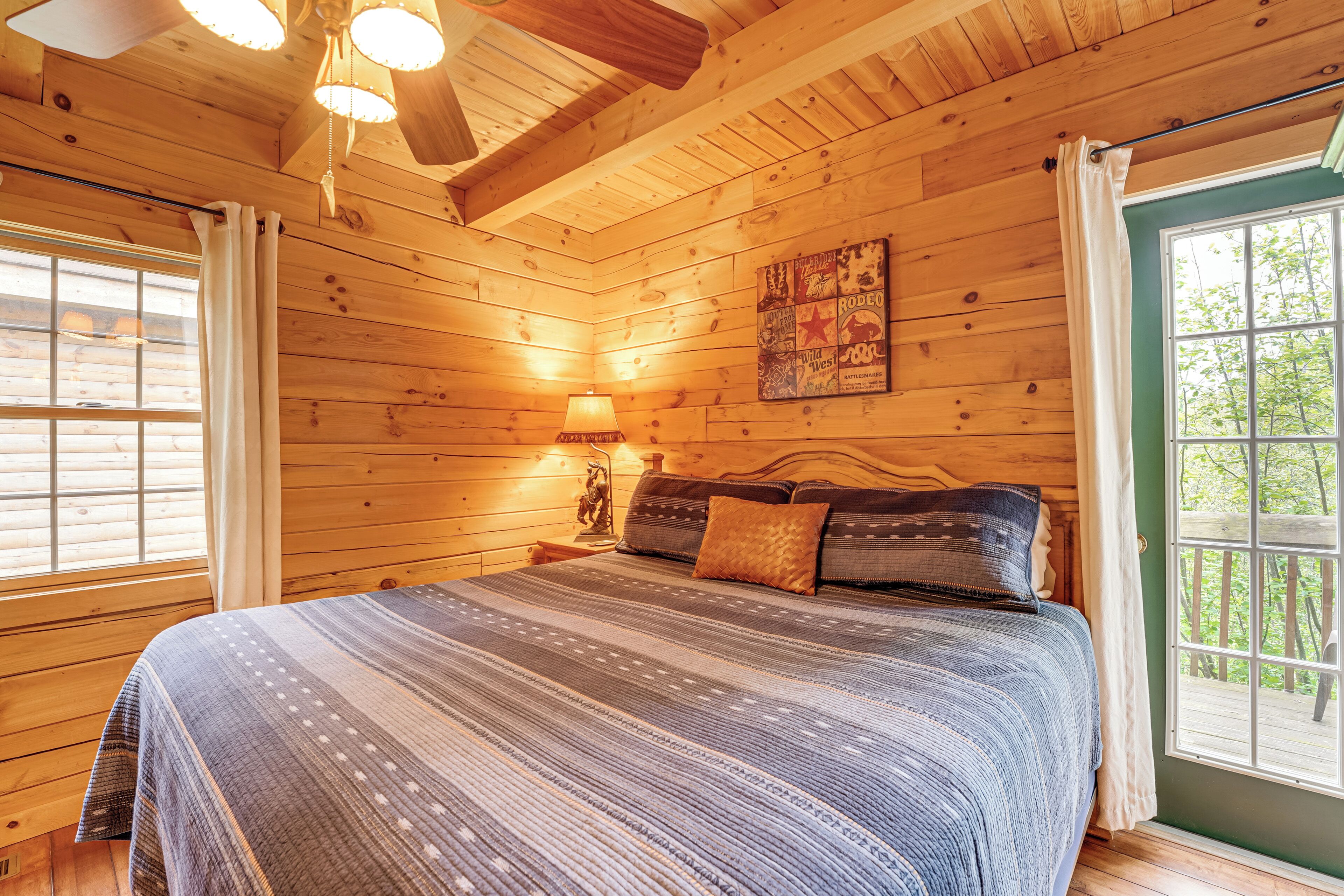 Quarto de cabana de madeira com cama, mesa de cabeceira, abajur e janela com cortinas.