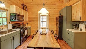 A wooden cabin kitchen with a wooden table, cabinets, a stove, and a refrigerator. - Fire Pit & Porch: Warm & Woodsy Rothbury Escape! (Rothbury)