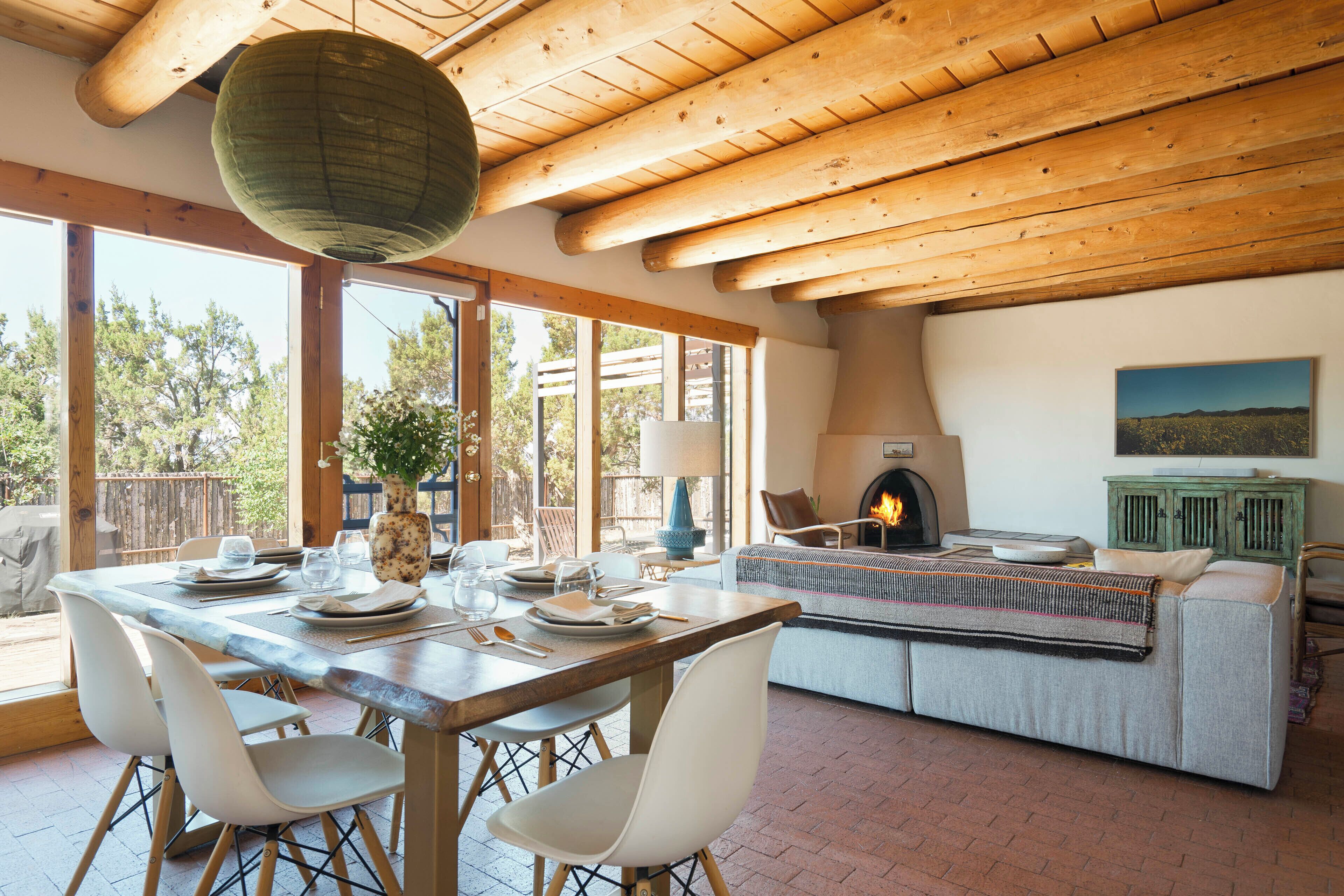 A dining area with a wooden table set for four, surrounded by white chairs, a fireplace, and a sofa with a throw blanket.