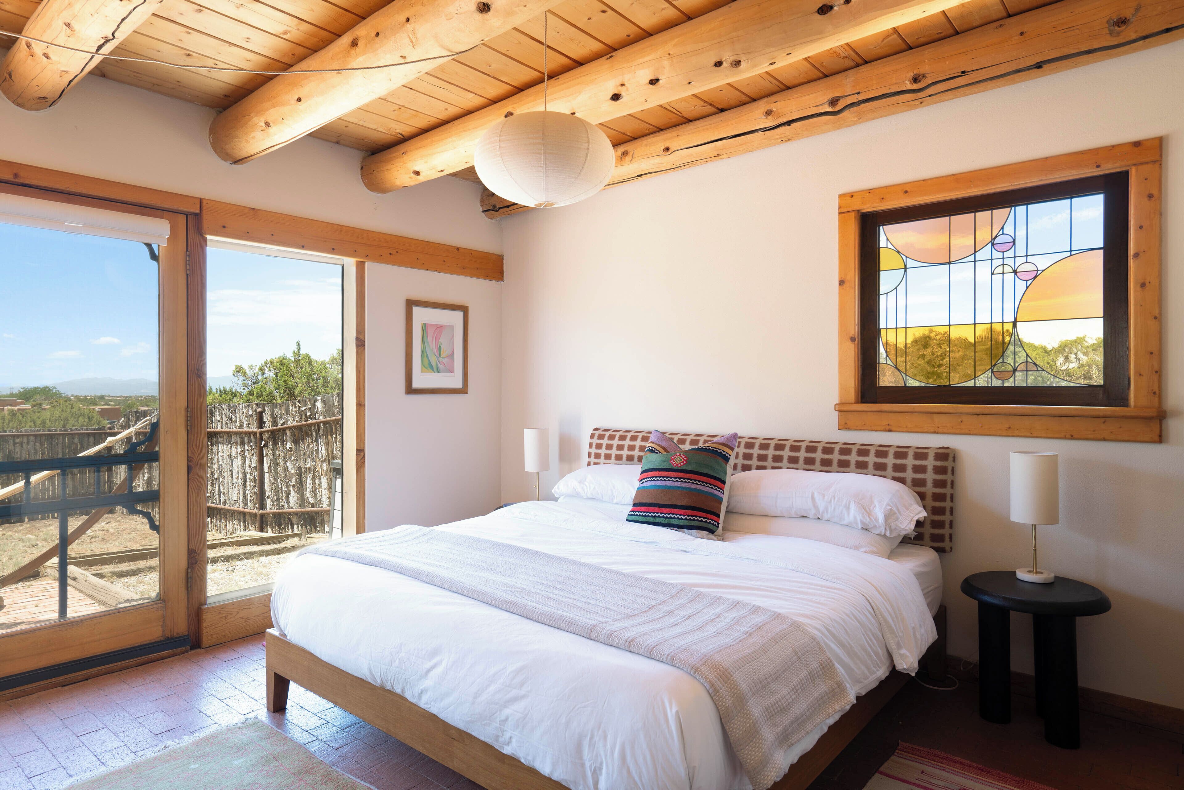 A bedroom with a bed, a window with a view, and a door leading to an outdoor area.