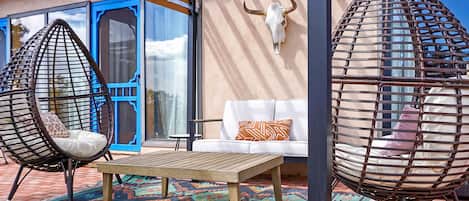 Eine Terrasse mit zwei Hängestühlen, einem Holztisch und einem weißen Sofa.