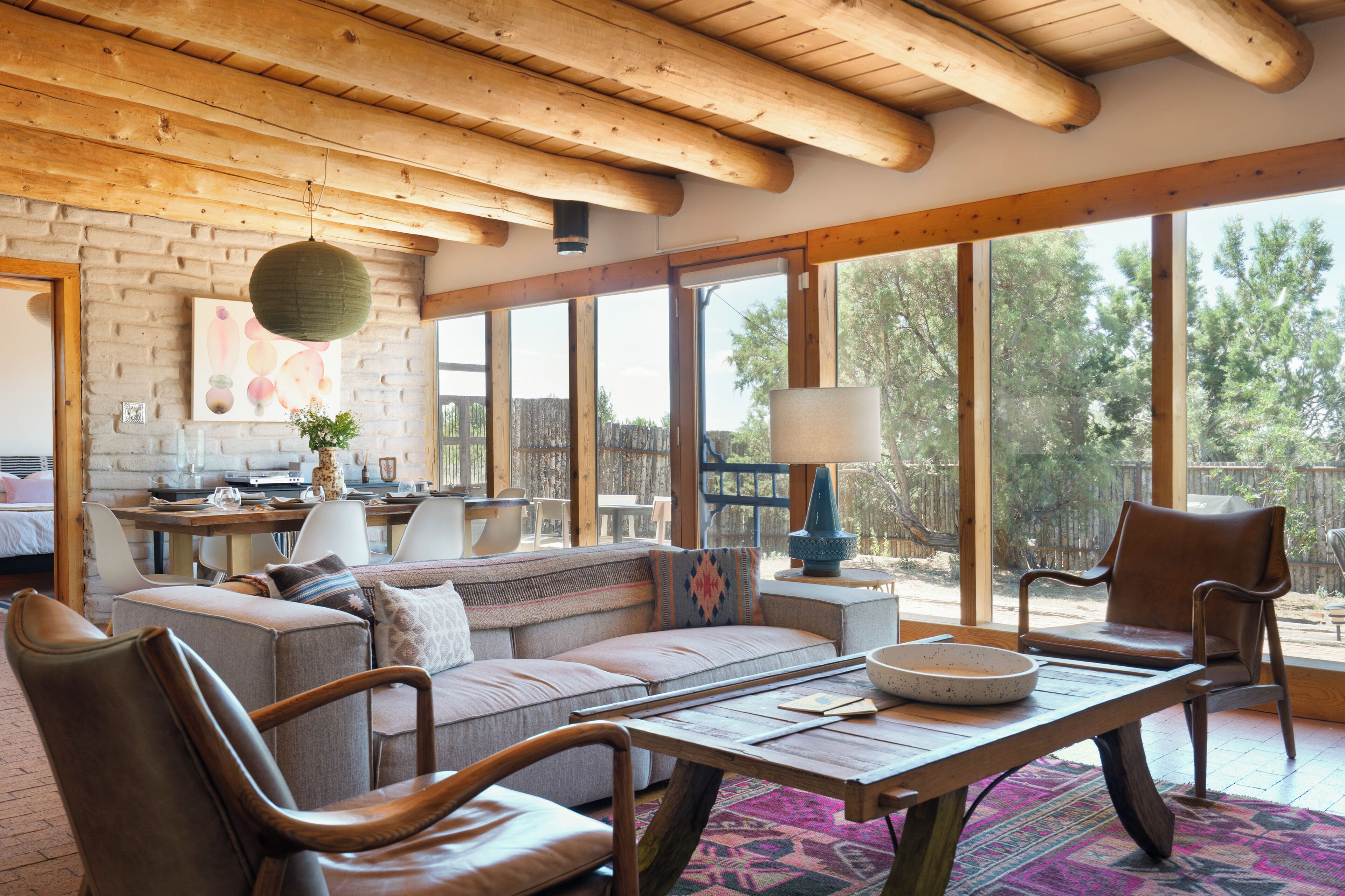 A spacious living area with a wooden ceiling, large windows, a sofa, chairs, and a dining table.