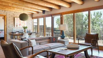 A spacious living area with a wooden ceiling, large windows, a sofa, chairs, and a dining table.