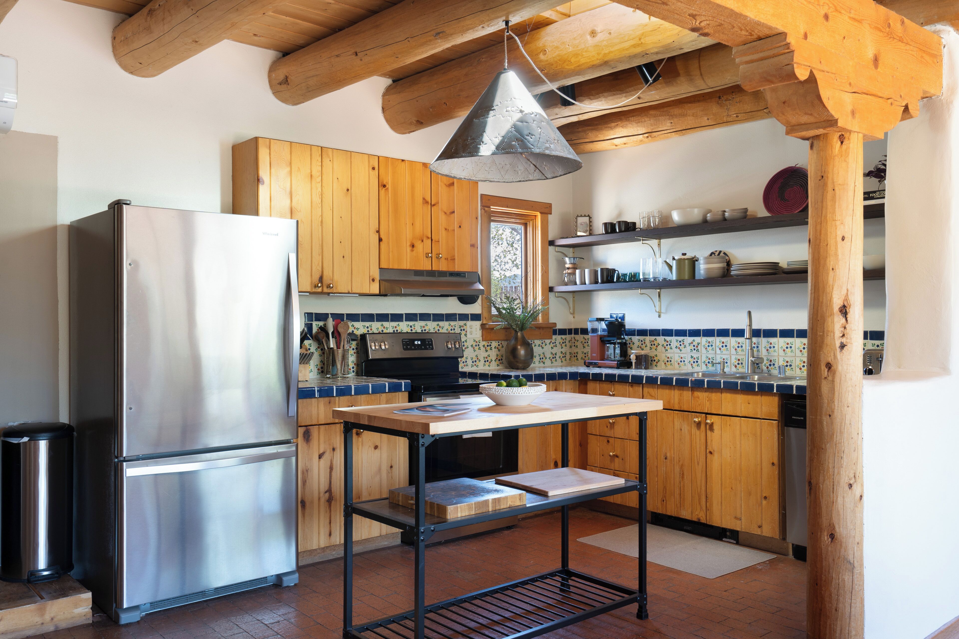 Una cocina con armarios de madera, un refrigerador de acero inoxidable, una estufa negra y una lámpara colgante.