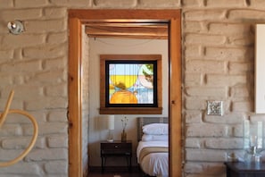 A room with a wooden-framed window, a bed, a bedside table, and a lamp.