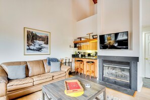 A living room with a fireplace, a sofa, a coffee table, and a kitchen area with bar stools.