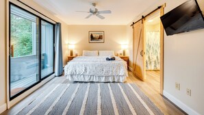 A bedroom with a large bed, sliding glass doors, a ceiling fan, a mounted TV, and a painting on the wall.