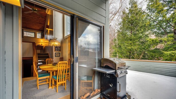 A covered deck with a grill, sliding glass doors leading to an indoor dining area with a table and chairs.