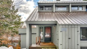 A modern house with a metal roof, a wooden front porch, and a green door.