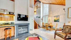 A spacious living area with a fireplace, wooden furniture, and a television mounted on the wall.