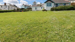 A grassy field with a picnic table and a house with a blue roof and white walls. - Beachcliff (St Austell)