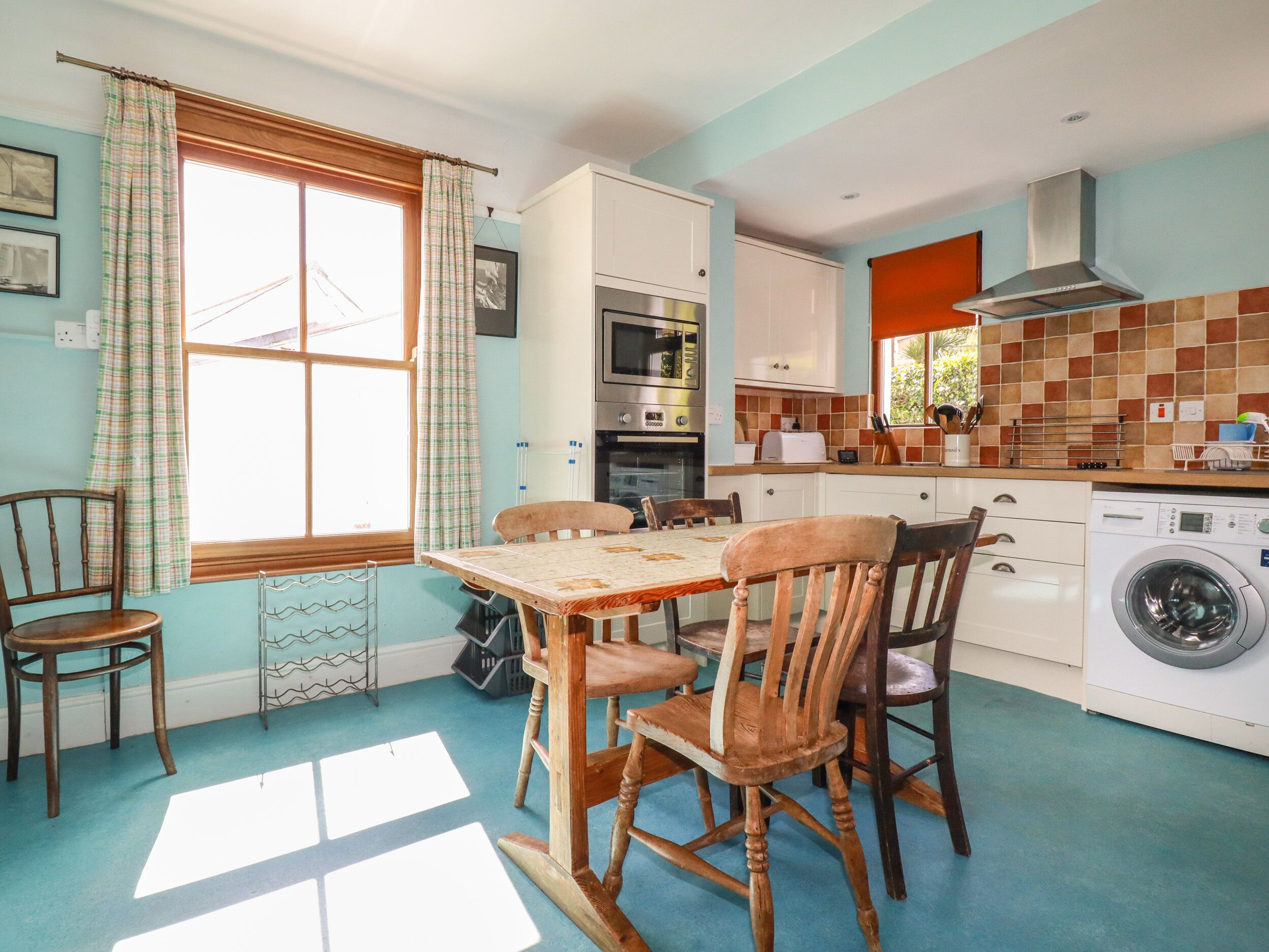 Una cocina con mesa, sillas, lavadora y ventana con cortinas.
