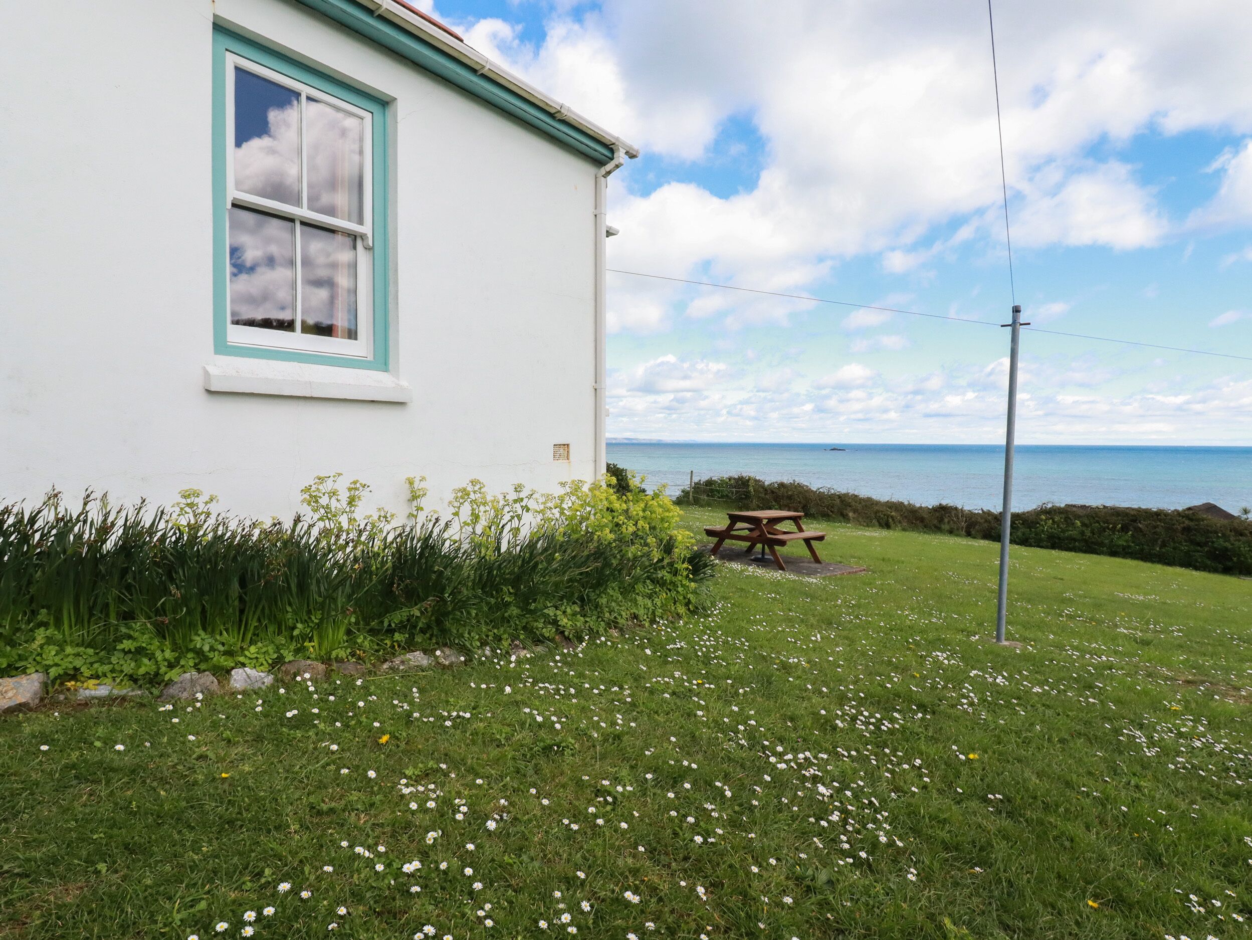 A white building with a blue window frame and a picnic table in front of a grassy area with white flowers.
