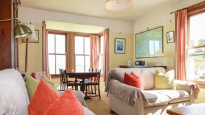 A well-lit living room with a sofa, a dining table, and a television. - Beachcliff (St Austell)