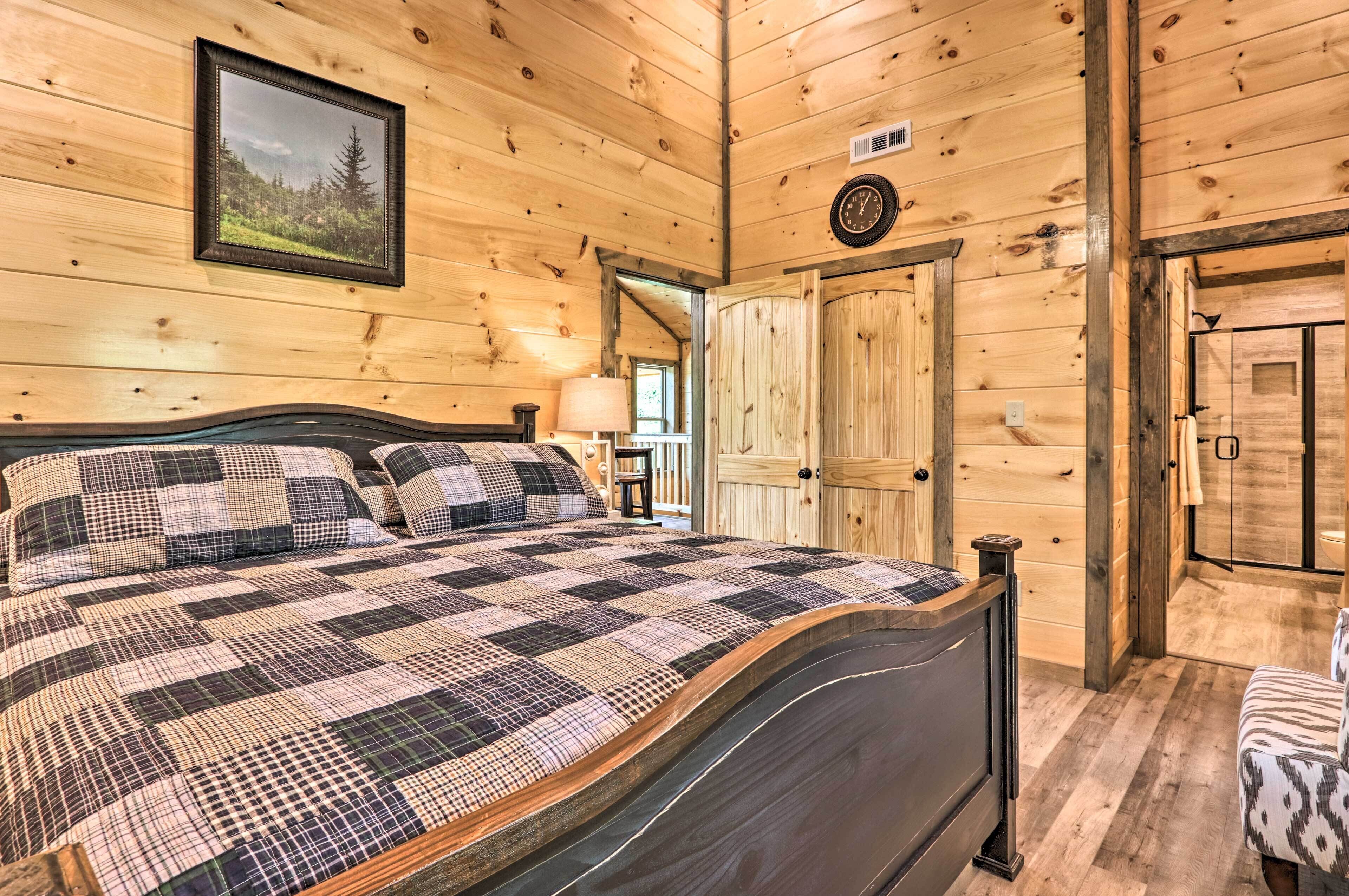 A wooden cabin bedroom with a large bed, a framed picture on the wall, and a door leading to another room.