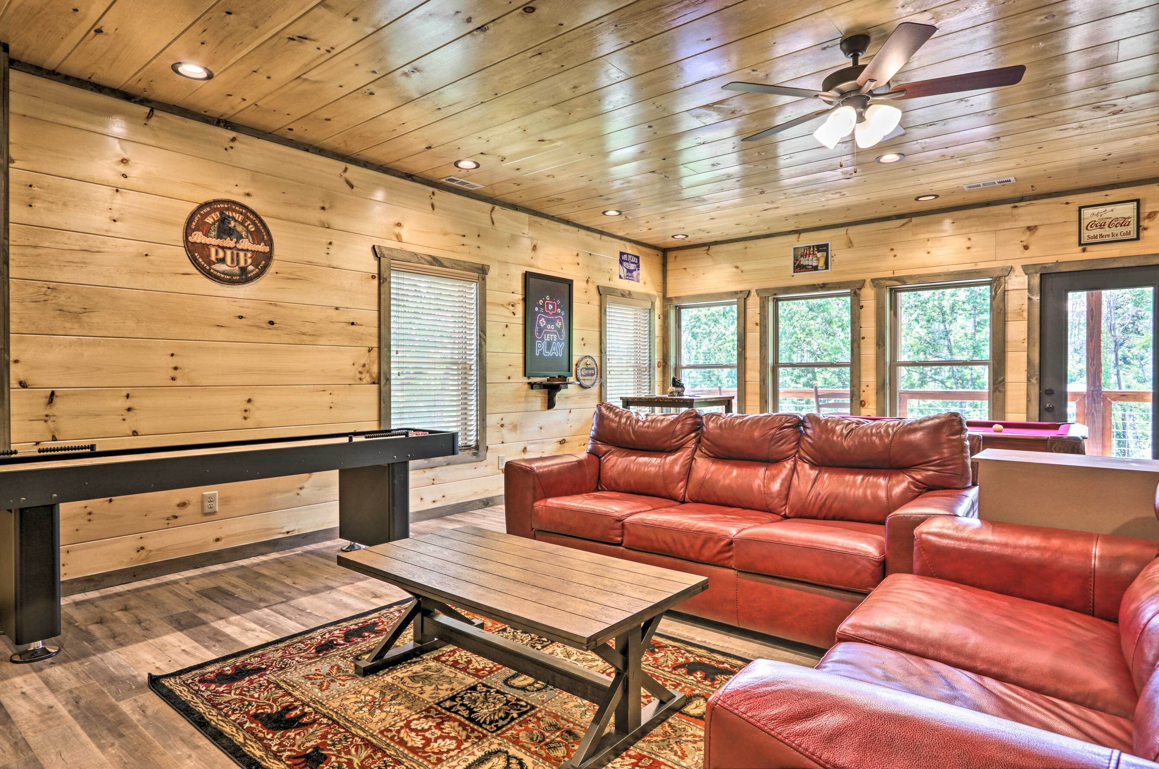 A cozy room with a pool table, leather sofa, and a ceiling fan.