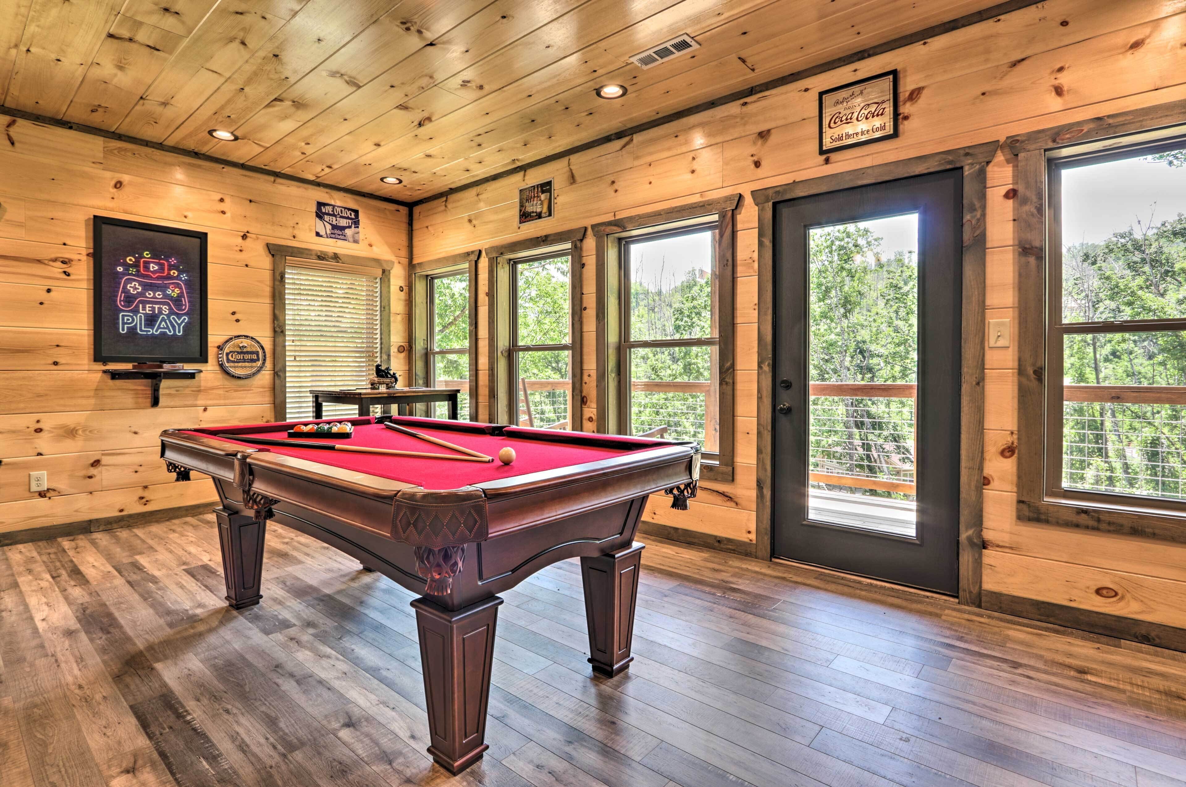 A pool table in a room with wooden walls and large windows.