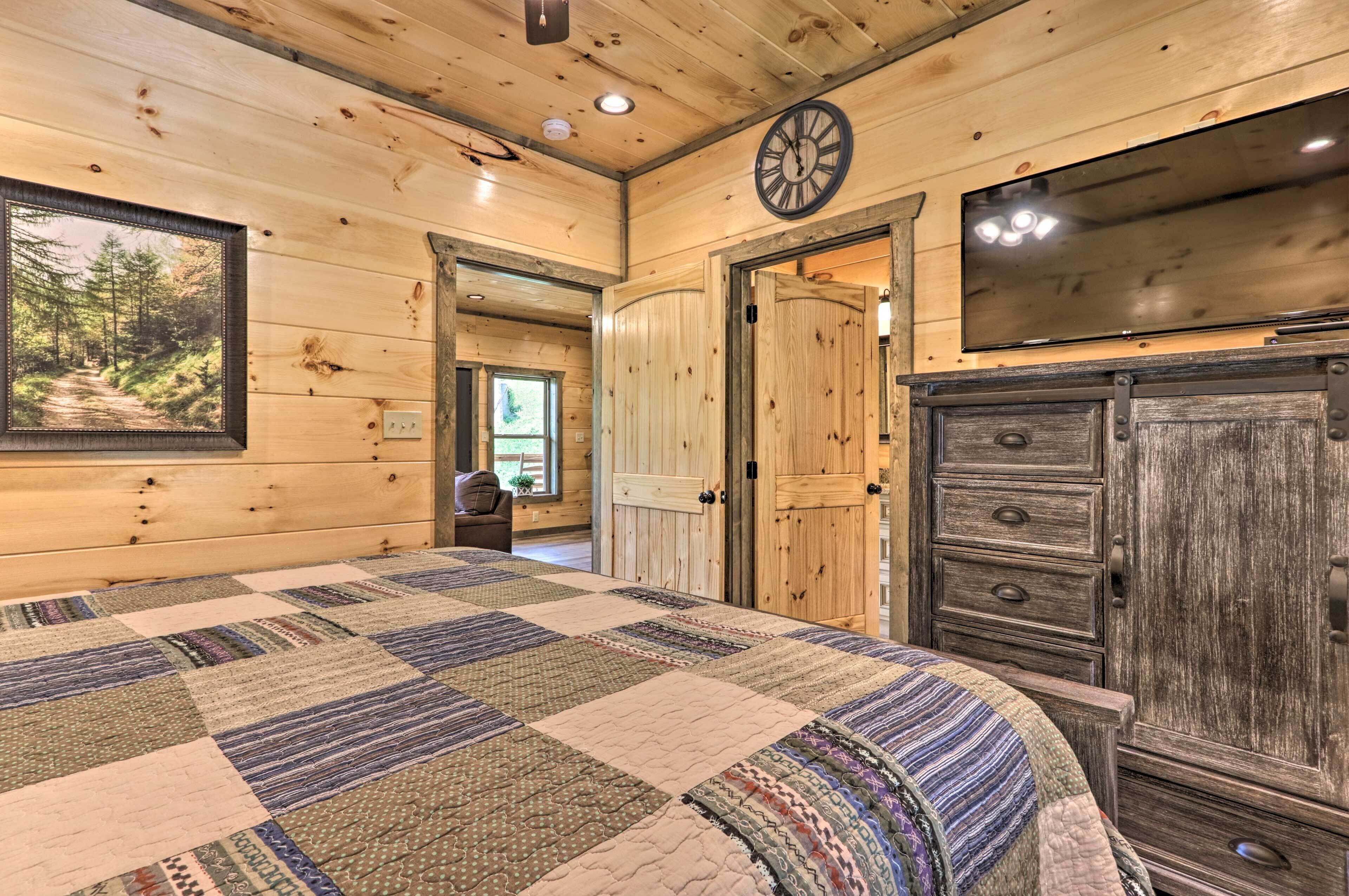 A wooden cabin interior with a large bed, a wooden wardrobe, a clock, and a television.