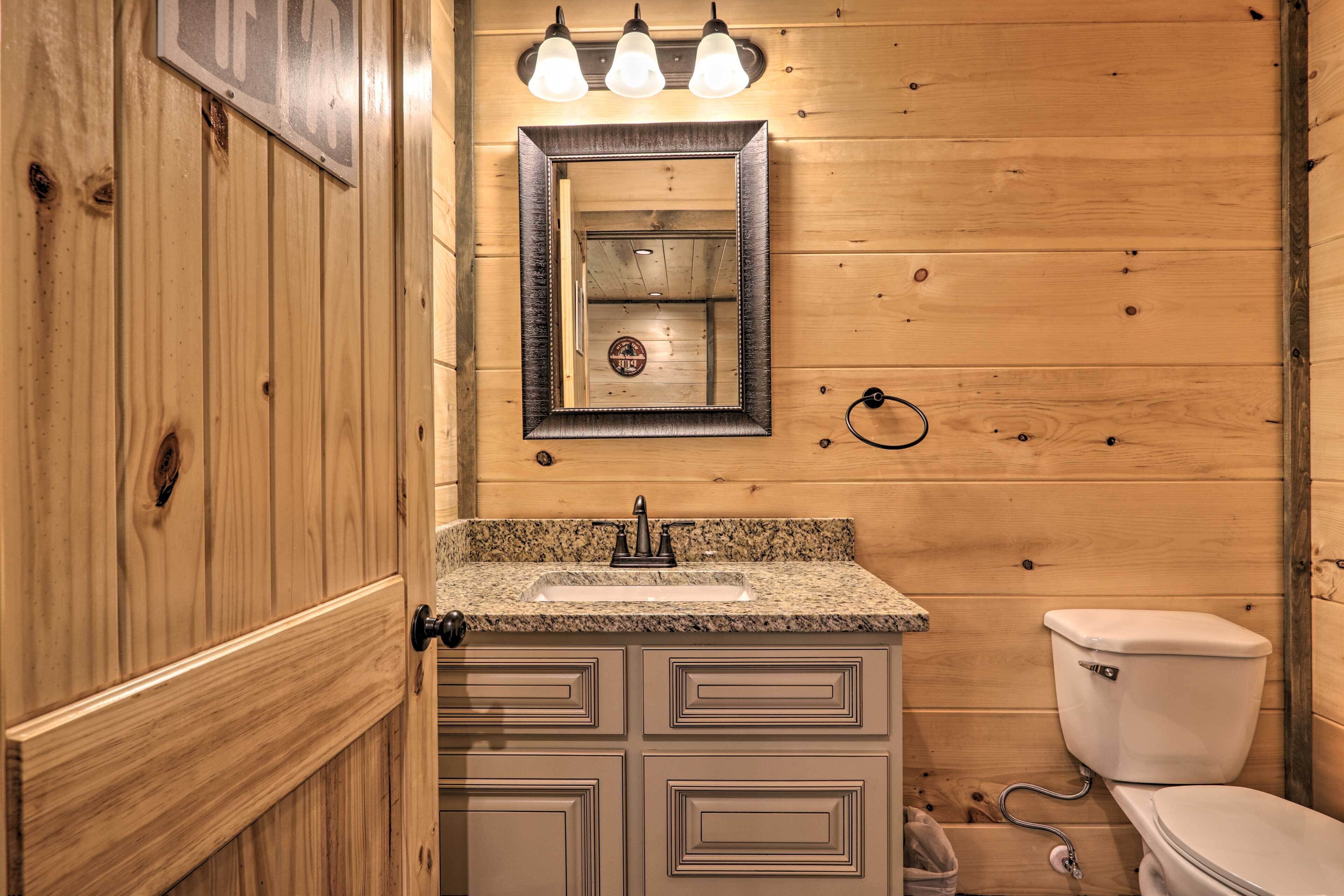 A wooden-paneled bathroom with a granite countertop sink, a mirror, and a toilet.