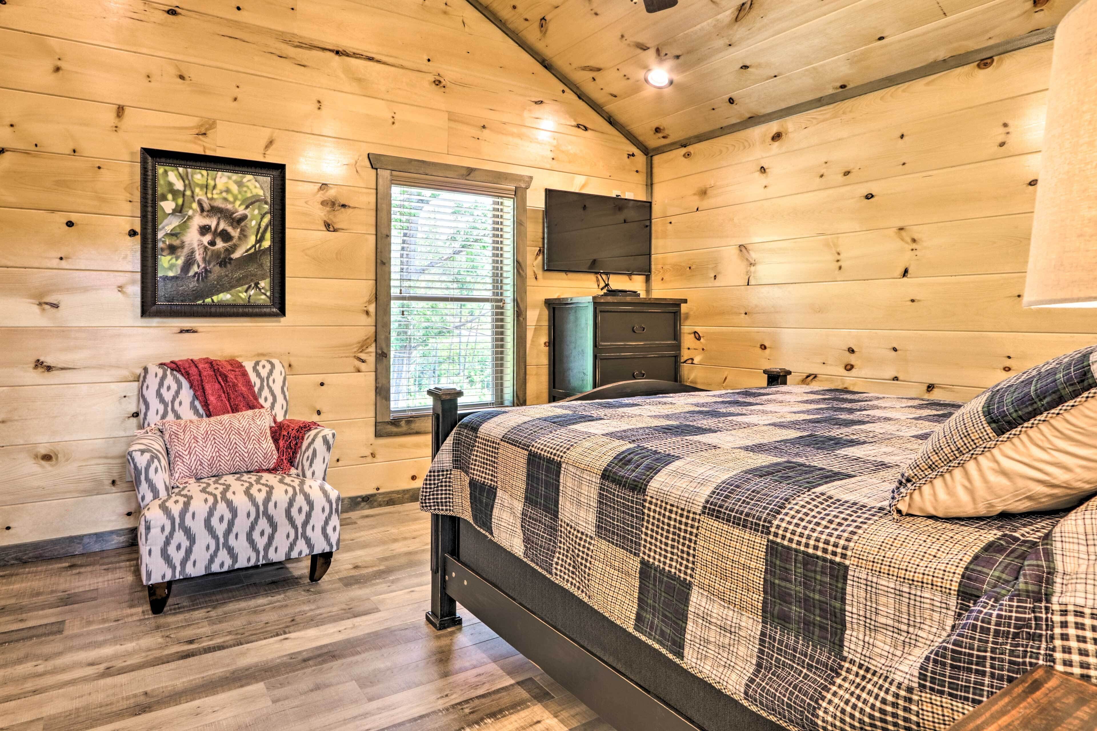A wooden cabin bedroom with a bed, a chair, a dresser, and a TV on the wall.