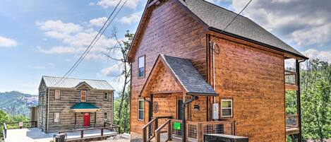 A rustic wooden cabin with a red door, a small porch, and a staircase leading to a balcony.