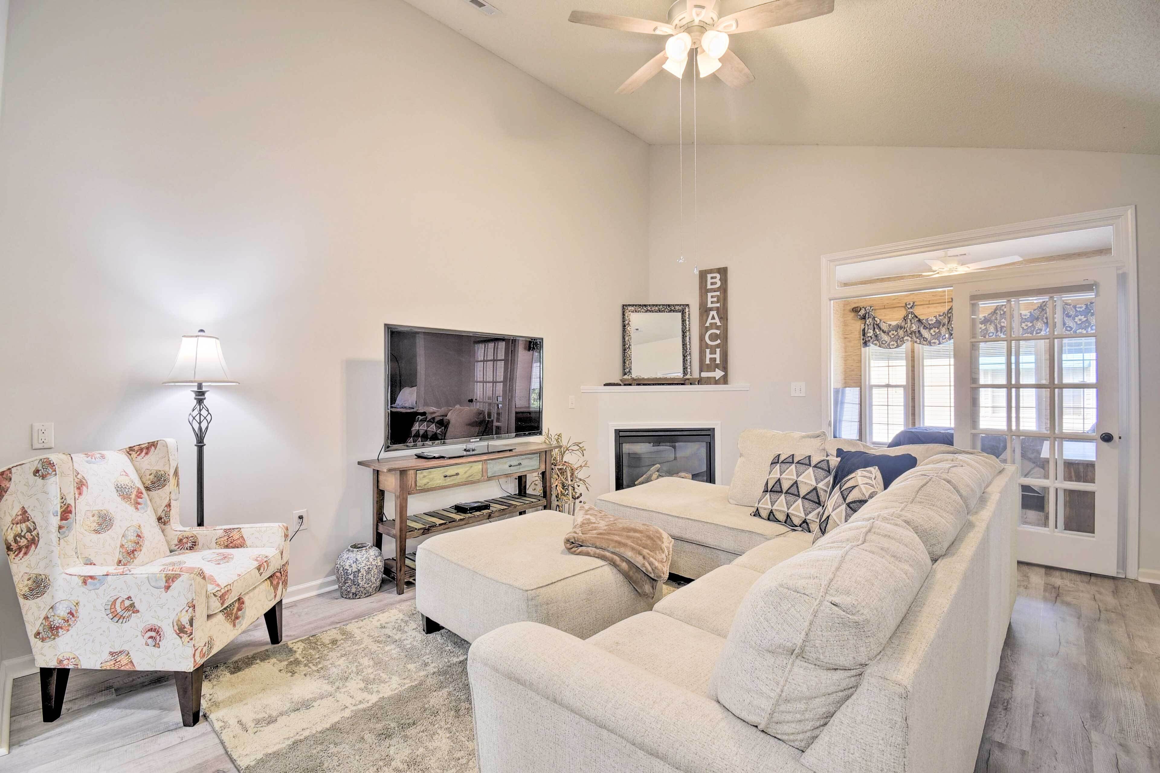 A living room with a sofa, armchair, TV, fireplace, and a sign indicating a beach direction.