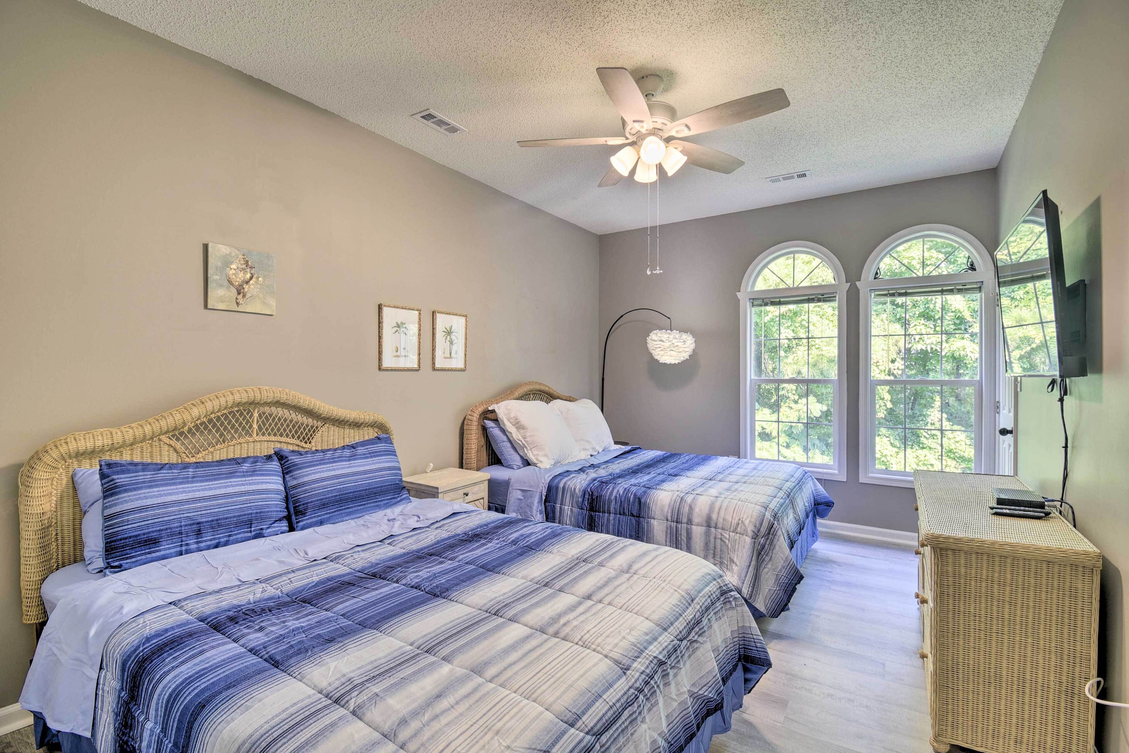 A bedroom with two beds, a ceiling fan, and large windows.