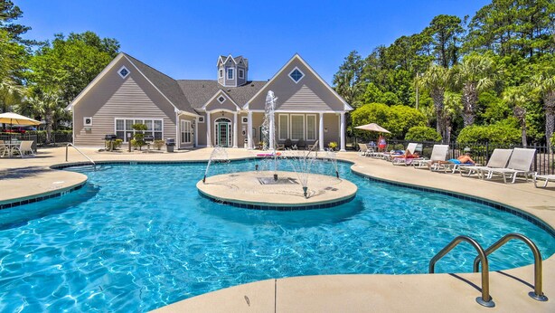 Une piscine avec une fontaine, entourée de chaises longues, et une maison en arrière-plan.