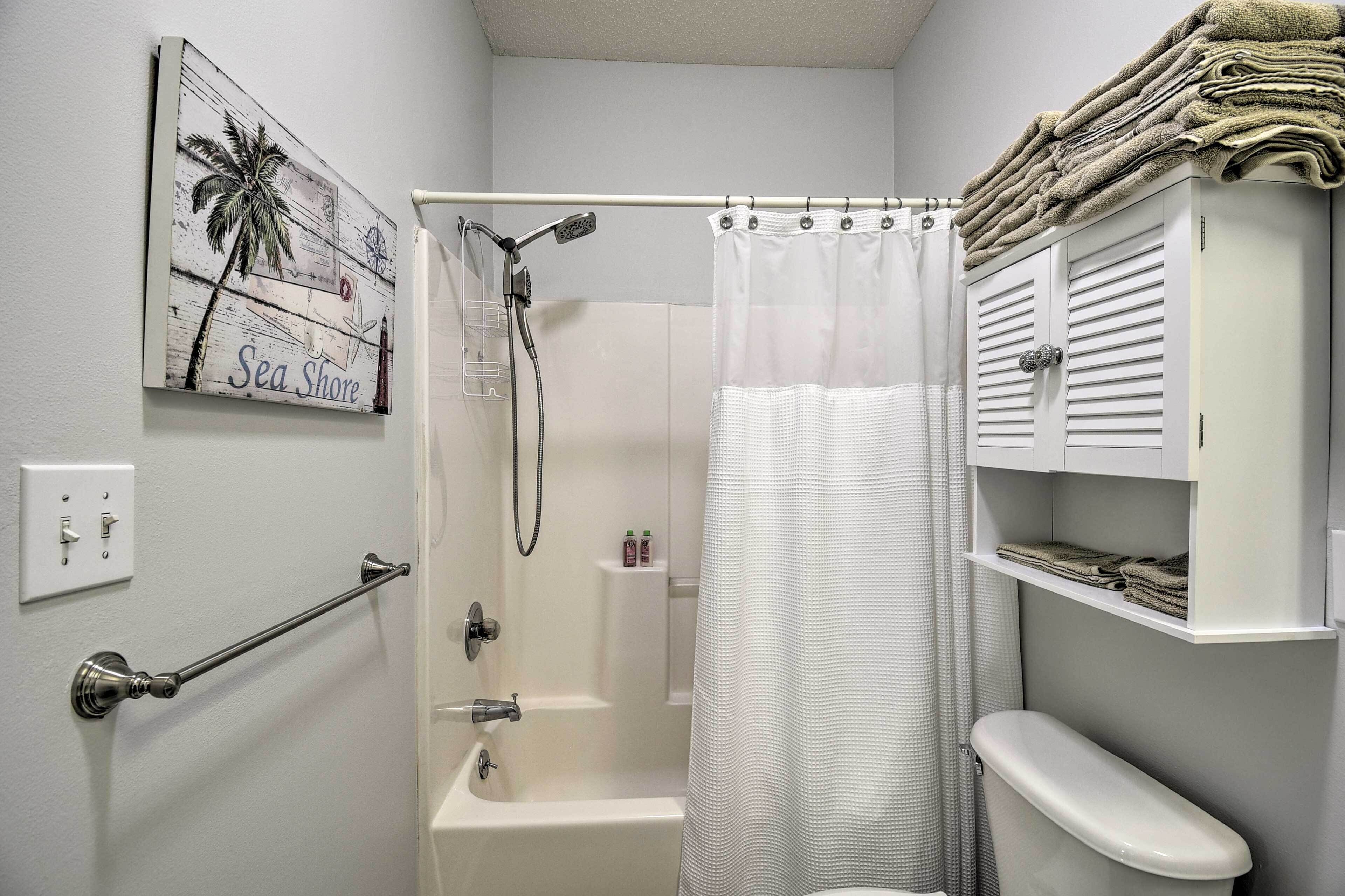 A bathroom with a shower, toilet, towel rack, and a wall-mounted towel shelf.