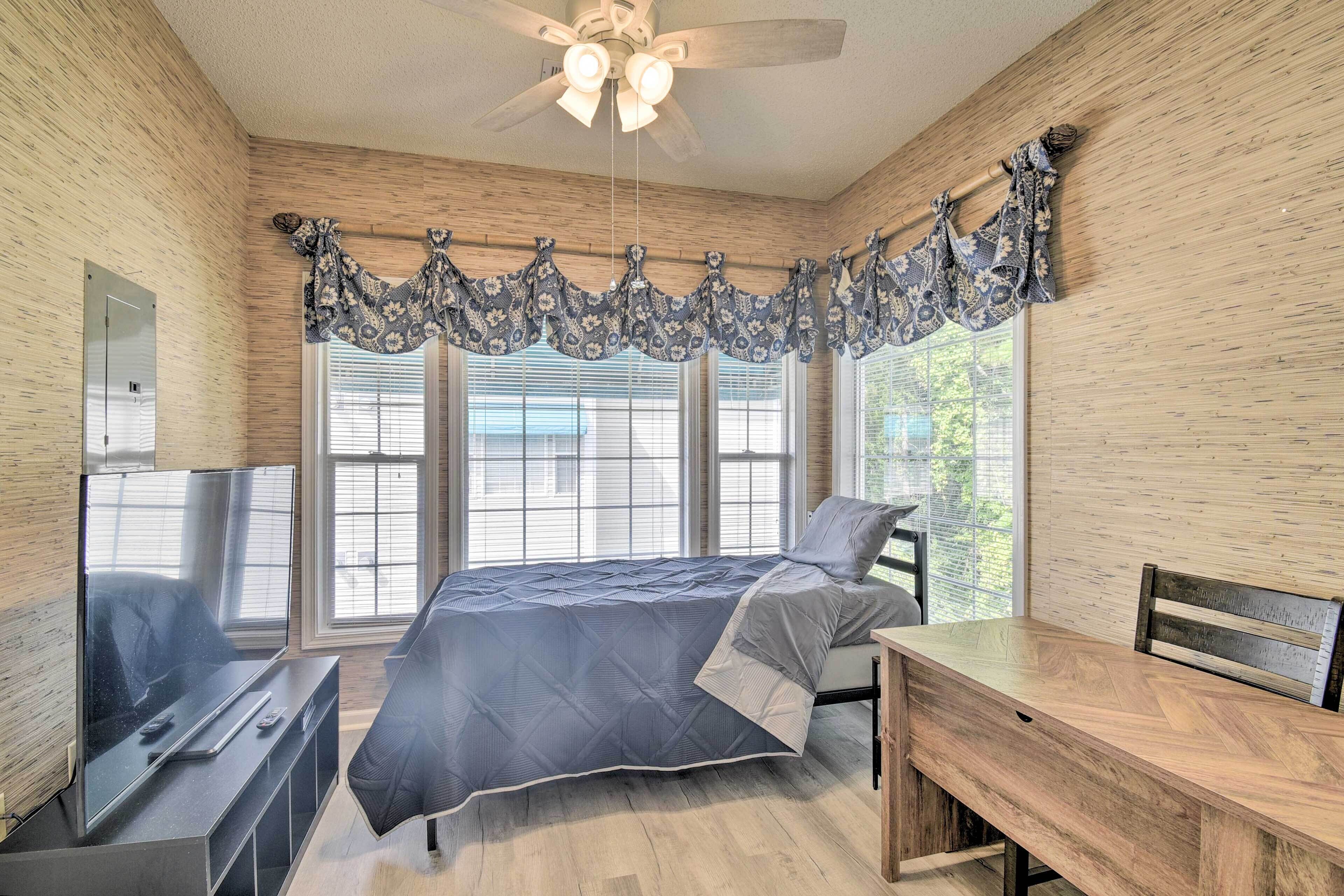 A bedroom with a bed, a desk, a chair, a TV, and a ceiling fan.