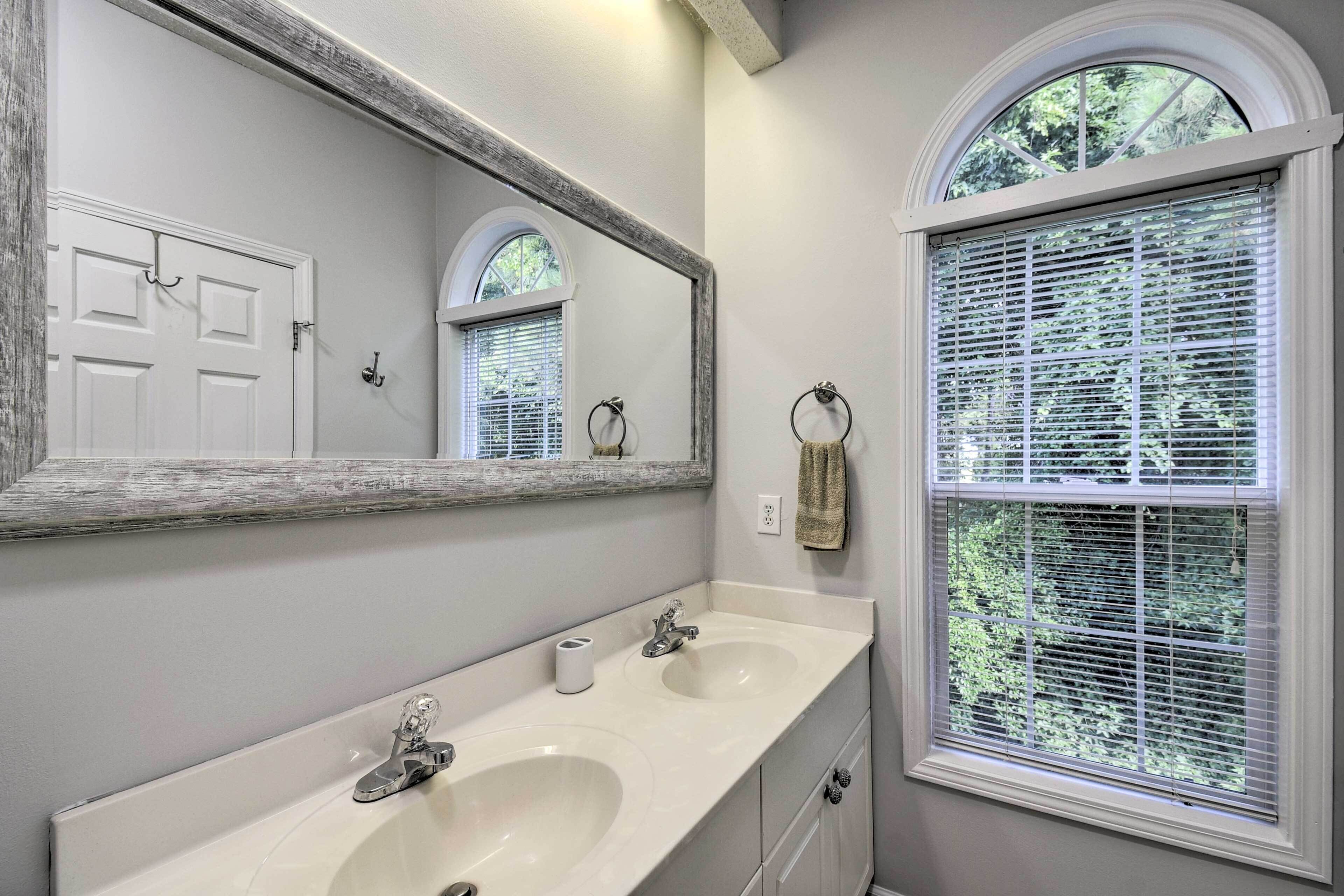 A bathroom with two sinks, a large mirror, and a window with blinds.