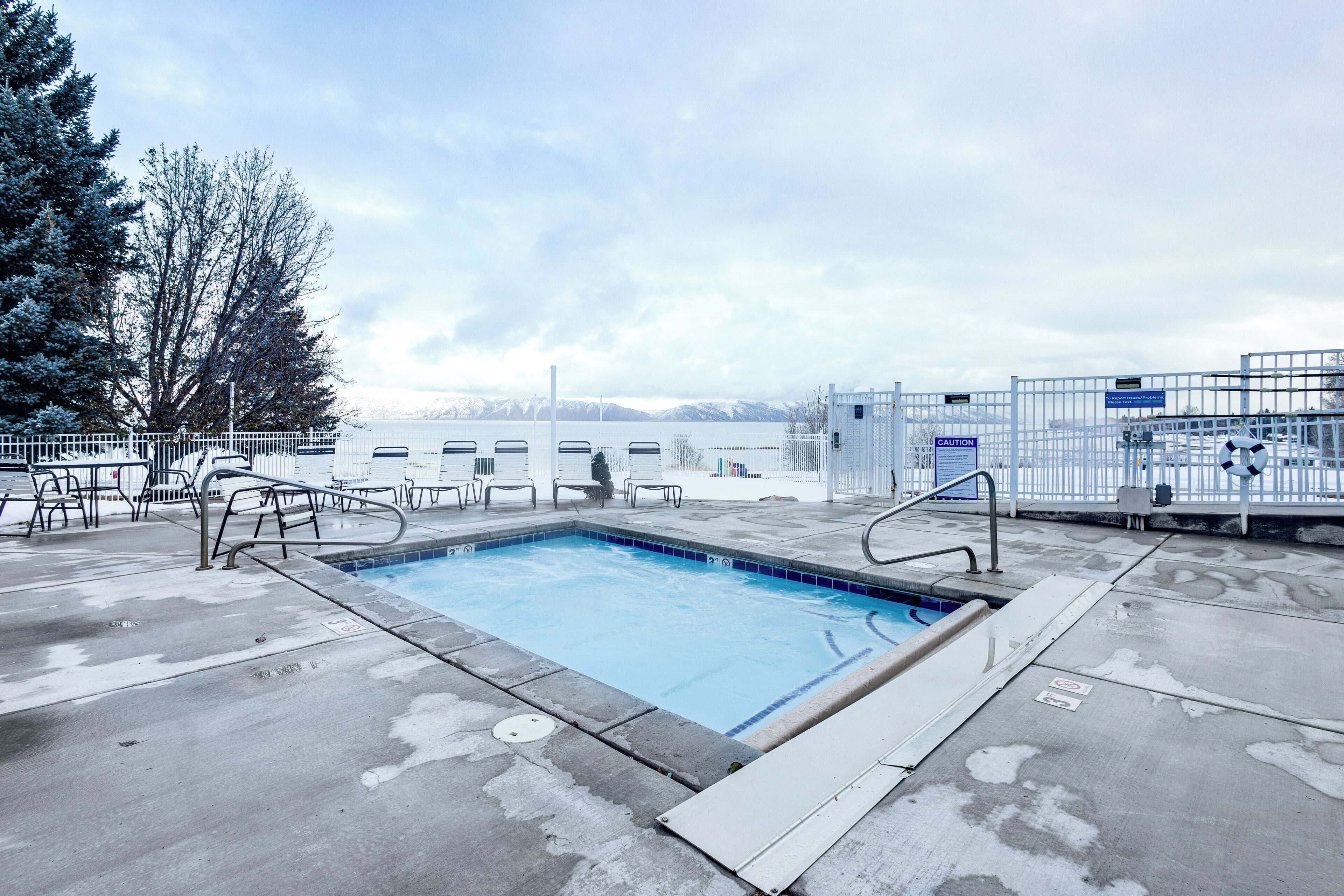 A rectangular pool with a blue interior, surrounded by a white metal fence, and a view of mountains in the background.