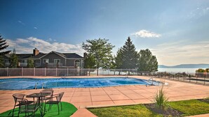 A swimming pool with a covered area, a patio with chairs, and a view of a body of water and mountains.