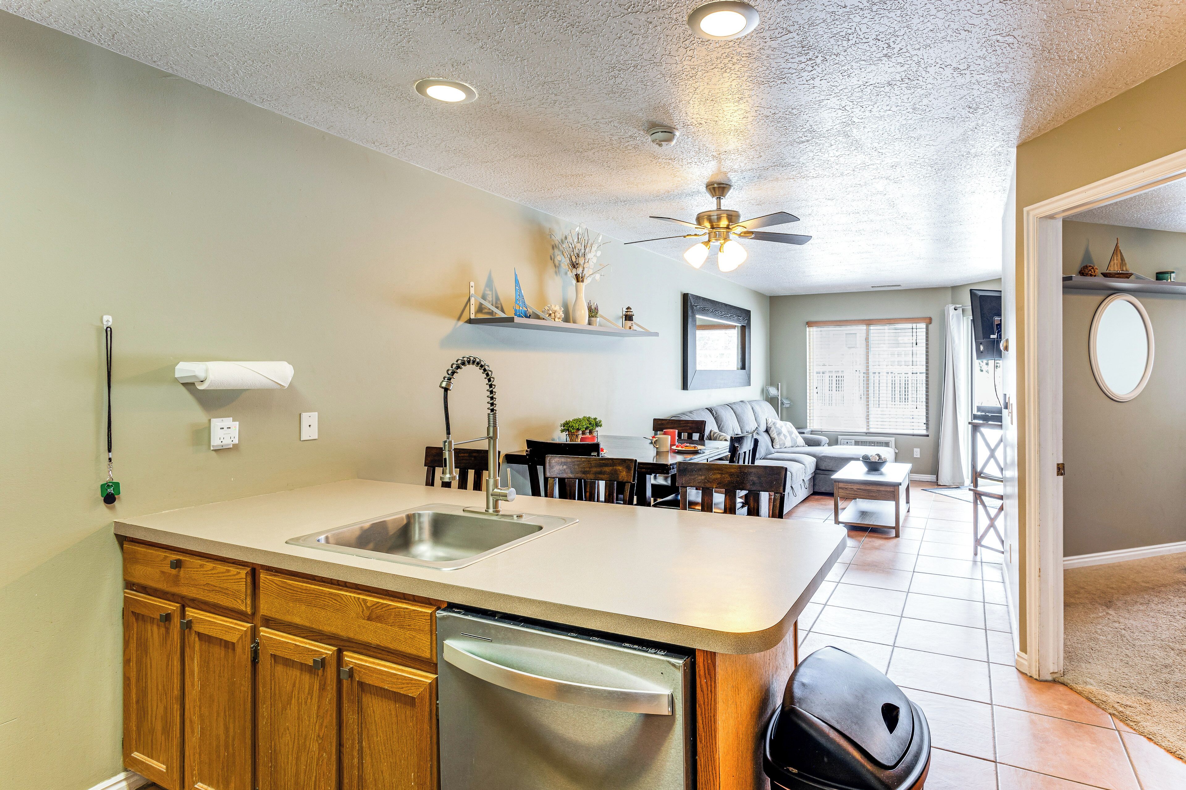 A kitchen with wooden cabinets, a dishwasher, and a countertop with a sink. There is a ceiling fan and recessed lighting.