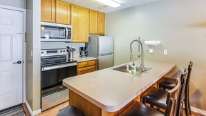 A compact kitchen with wooden cabinets, a microwave, stove, refrigerator, and a sink with a faucet.