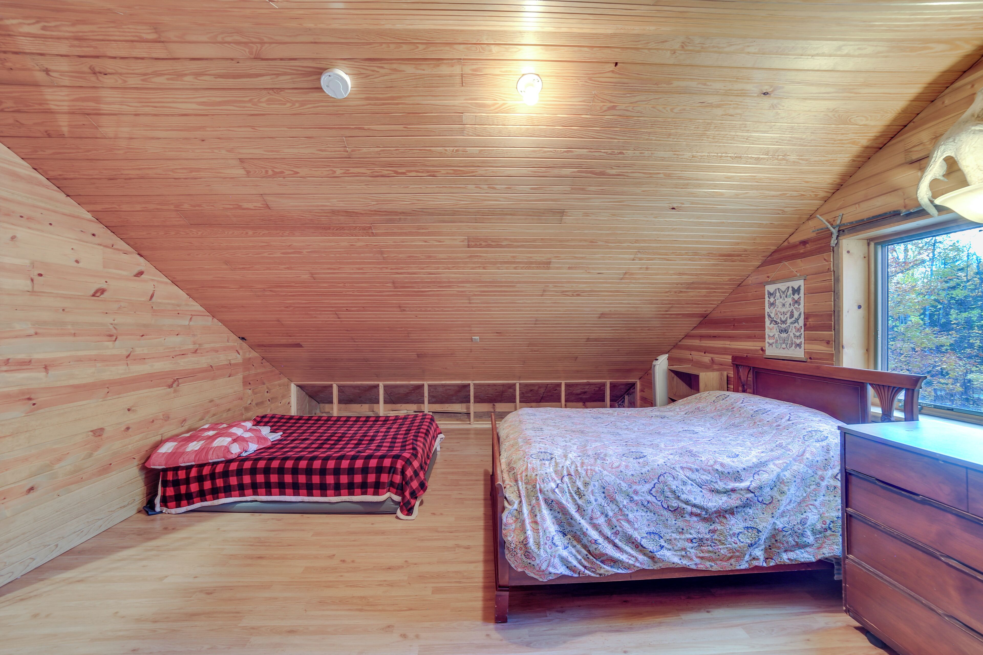 A wooden cabin bedroom with two beds, a dresser, and a window with a view of trees.