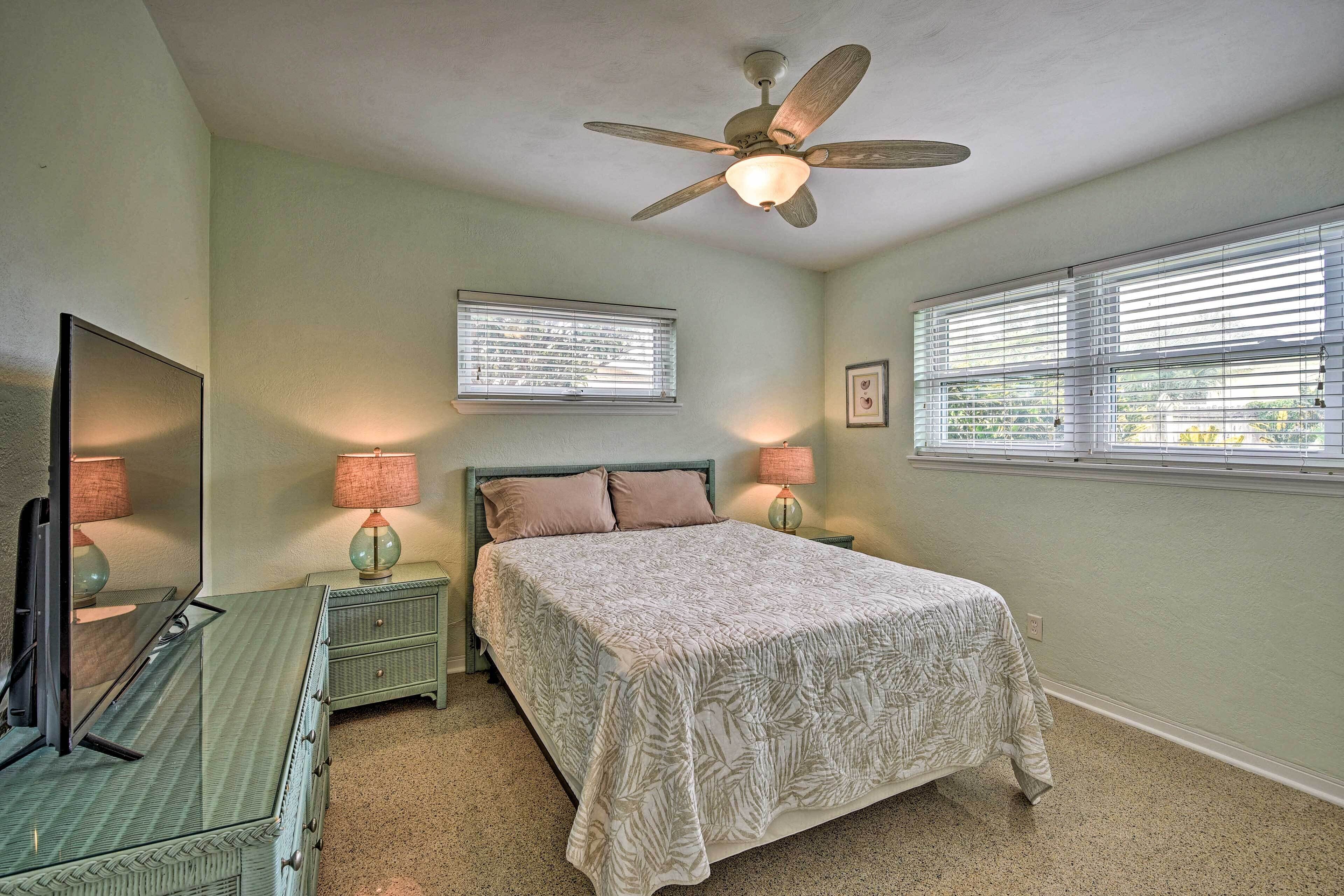 A bedroom with a bed, a ceiling fan, a dresser, a TV, and two bedside lamps.