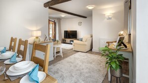 A dining area with a wooden table set for four, a sofa, and a television in the background. - Manor Farm Barn Cottage - Close Lake District & Yorkshire Dales (Yealand Conyers)