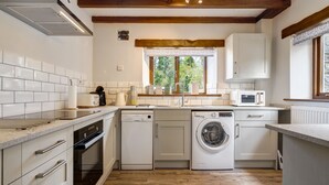 A compact kitchen with white cabinetry, a built-in dishwasher, a washing machine, and a microwave. - Manor Farm Barn Cottage - Close Lake District & Yorkshire Dales (Yealand Conyers)