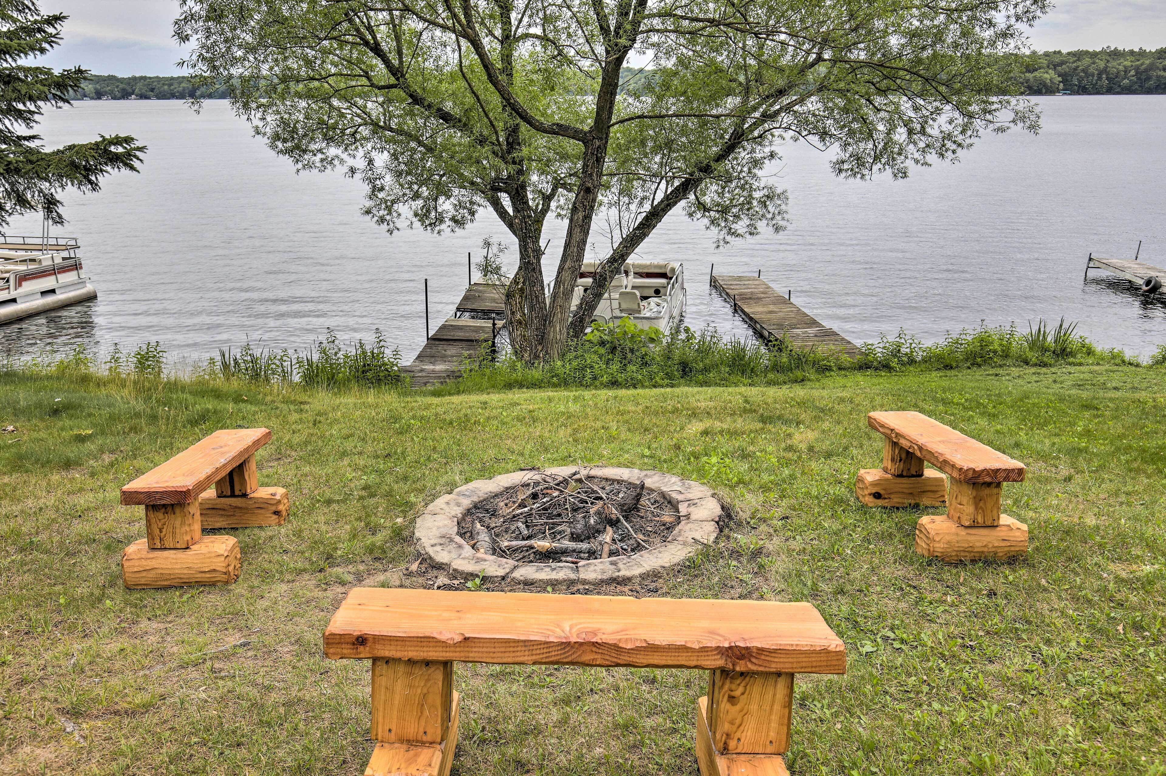 A lakeside picnic area with wooden benches and a fire pit.