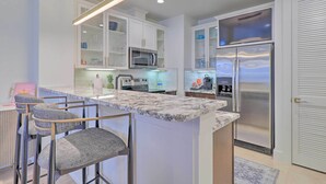 A modern kitchen with white cabinets, a stainless steel refrigerator, and a marble countertop. - Lake LBJ Condo w/ Balcony & Shared Boat Docks (Horseshoe Bay)