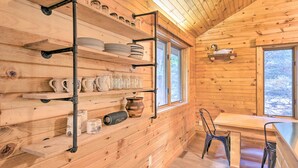 A wooden cabin interior with shelves holding dishes, cups, and jars, a table with chairs, and a window with a view of trees. - Waterfront Cottage w/ Dock on Papoose Lake! (Manitowish Waters)