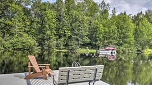 A dock with a wooden chair and a bench, a calm lake, and a forested area in the background. - Waterfront Cottage w/ Dock on Papoose Lake! (Manitowish Waters)